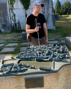Cédric debout devant le plan de la ville de Soleure. Ce dernier est en 3D et comporte des indications en braille.